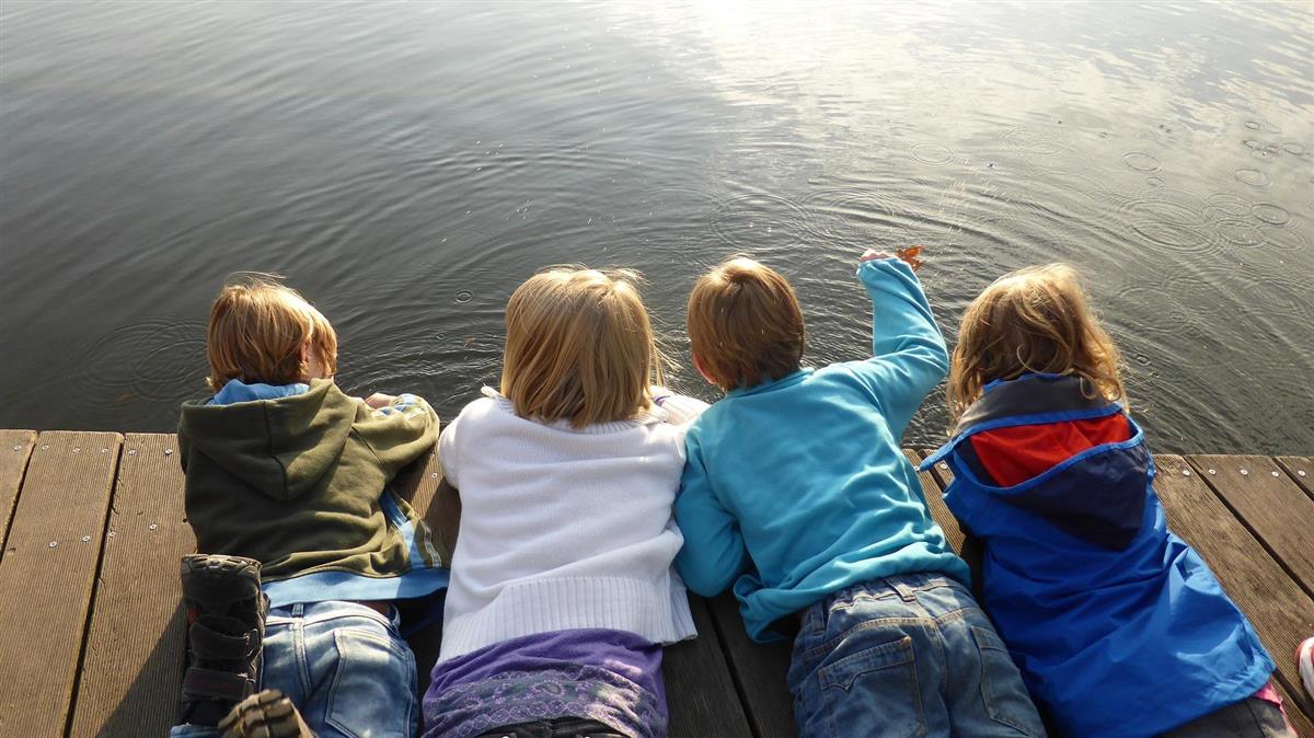 Illustrasjonsfoto av barn som ligger på brygge og ser ned i vannet. - Klikk for stort bilde