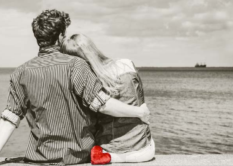 Illutrasjonsbilde av mann og kvinne som sitter på brygge og ser ut over havet. Bildet er i svart hvitt, og det er et rødt hjerte nærmest. - Klikk for stort bilde